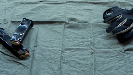 Black steel handgun pistol magazines loaded with hollow point ammunition and black and tan tactical gloves, resting on an olive drab cloth backgroundの写真素材