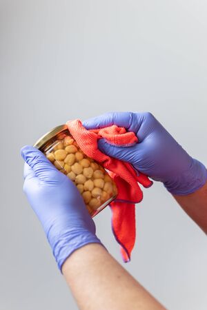 Gloved hands cleaning a jar of chickpeas after grocery shopping to prevent the spread of the coronavirusの写真素材