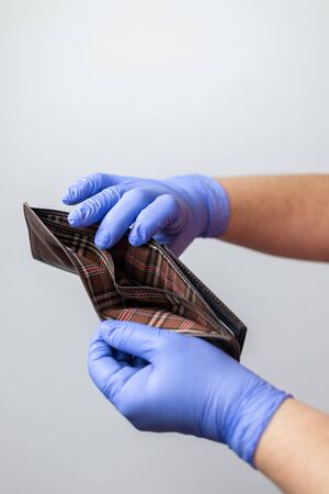 two hands with blue gloves showing an empty wallet. Concept of financial crisis due to the...