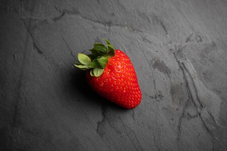 One strawberry on a black stone background, dark food photographyの写真素材