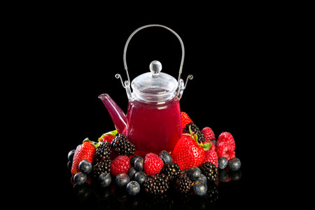 Glass teapot with red tea next to a selection of red fruits and berries on a dark backgroundの写真素材
