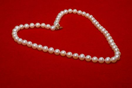 A beautiful heart shaped pearl Necklace on a red felt backgroundの写真素材