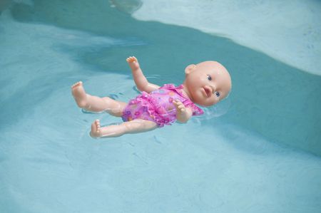 Toy baby doll floating in a swimming pool on its backの写真素材