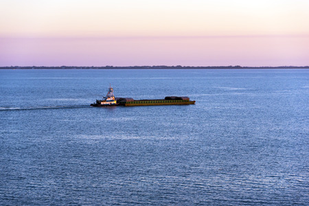 Tugboat pushing a barge across tampa bay at sunsetの写真素材