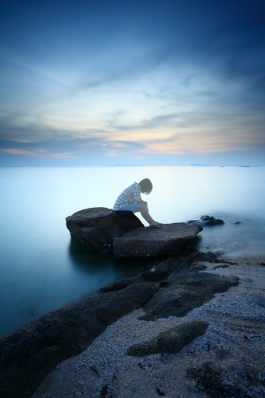 Woman  sitting and contemplating alon on the rock by the beachの写真素材
