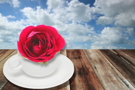 Red rose and white coffee cup on wood board with sky backgroundの写真素材