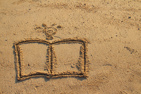 Book and light bulb drawn on sand beachの写真素材