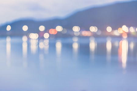 Colorful city lights with bokeh effect reflected over sea  background at dusk