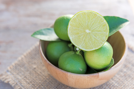 Fresh branch of limes in wood bowl on old wooden table backgroundの写真素材