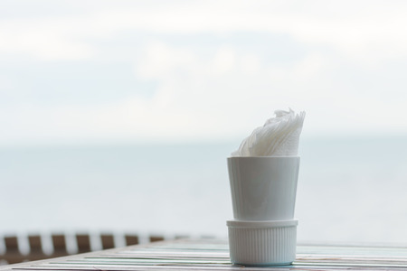 Napkins in white cup on retro wood table with blue blurred sea sky backgroundの写真素材