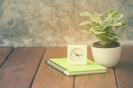 wooden work table with notebook,alarm clock and fresh green tree in vase potの写真素材