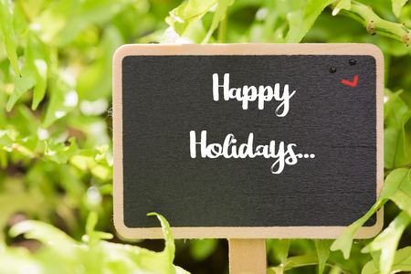 Happy holidays text on blackboard over green field backgroundの写真素材