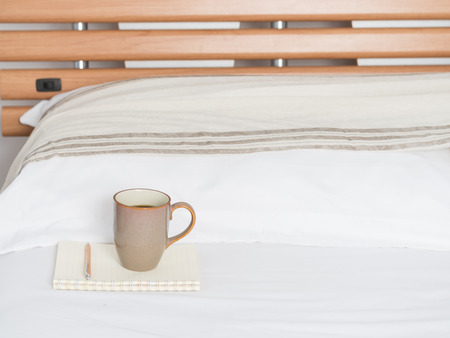 Cup of coffee and notebook memo on cozy white bed  room