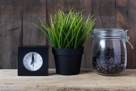 Coffee bar,roasted coffee beans,green grass pot,black alarm clock on grunge wooden table backgroundの写真素材