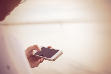 Teenager girl using mobile phone over sea landscape background,retro efffectの写真素材