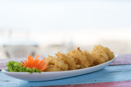 Deep batter fried squid rings calamari on vintage wood table with blurred white beach backgroundの写真素材