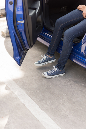 A women in blue jeans and sneakers shoes sit on blue car with door openの写真素材