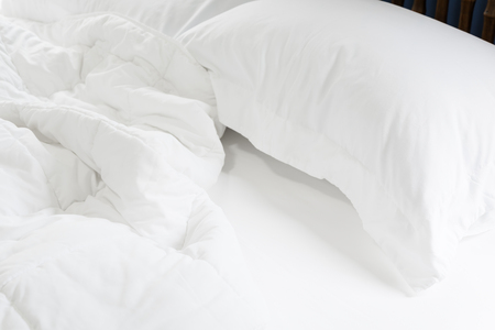 Close up messy white sheet and pillows on bed bedroom interiorの写真素材