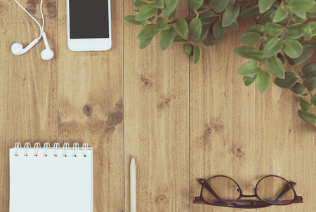 Minimal workspace,smartphone,notebook,pencil,green plant,earhead and eyeglass on wood table,top viewの写真素材