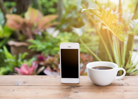 Morning outdoor work,coffee cup,mobile phone on wooden table in green garden backgroundの写真素材