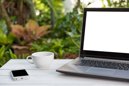 Computer laptop,mobile phone and coffee cup  on white  wooden table with green garden nature backgroundの写真素材