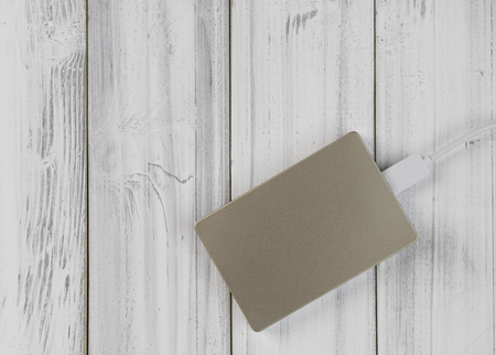 Flat lay design bronze colour external hard drive on white wooden background,top view