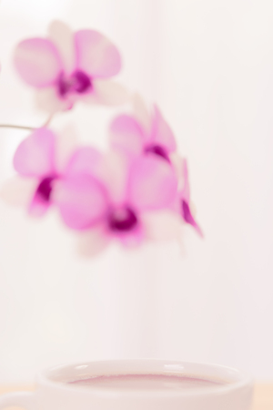 Coffee cup and beautiful purple orchid flowers on wood table over soft white background,pastel filterの写真素材