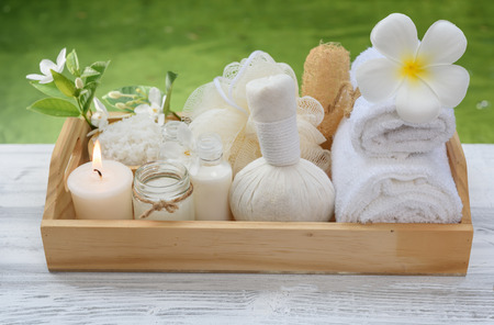 Spa wellness concept,white candle,milk soap,salt,towel,flowers and herbal massage ball on white wood table with green pond backgroundの写真素材