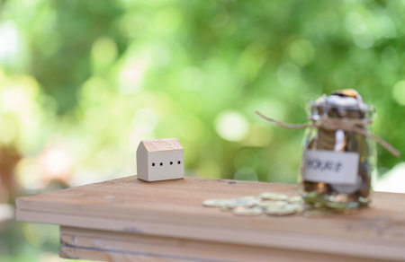 Saving money for house,coins in glass jar with quote house on wood table with pastel blurred backgroundの写真素材