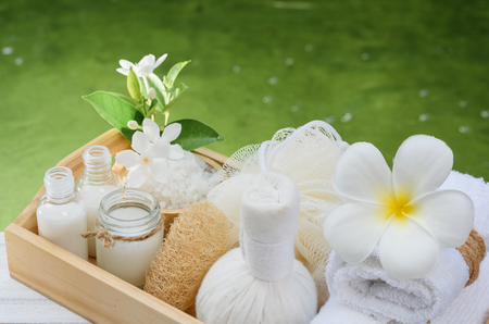 Spa wellness concept,white candle,milk soap,salt,towel,flowers and herbal massage ball on white wood table with green pond backgroundの写真素材