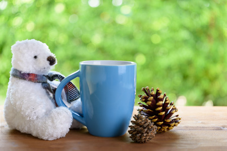 Blue coffee cup,cute teddy bear and pine cone on wood table top with green blurred backgroundの写真素材