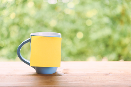 Blue coffee cup and sticky note for text on wood table top with green blurred backgroundの写真素材