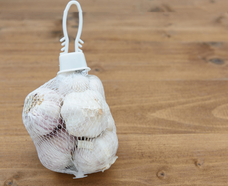 Garlic bulbs in white net package  on wooden table backgroundの写真素材