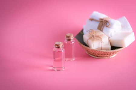 Spa wellness concept,rose liquid bottle,milk soap,white towels in wooden tray on pink backgroundの写真素材
