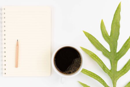 Office workspace desk with black coffee, notebook,pencil and green leaf  on white background,top viewの写真素材