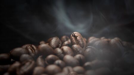 Aroma roasted coffee beans with smoke rising over dark backgroundの写真素材