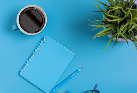 Work space blue set of note pad,pen,eyeglasses and coffee cup on blue desk background,top viewの写真素材