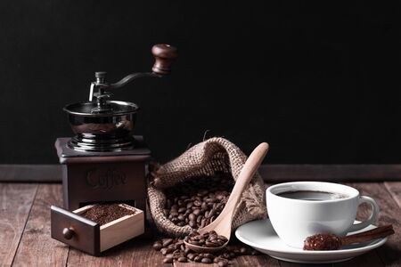 White coffee cup,coffee grinder and coffee beens in burlap  on wood table  with black  wall background の写真素材