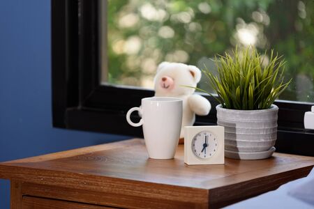 A teddy bear,coffee cup and white alarm on wood table in blue bedroomの写真素材