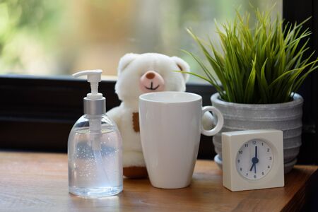 Hand sanitizer,white cup,teddy bear and alarm clock on wood table with green nature background while Covid-19  home quarantine .の写真素材