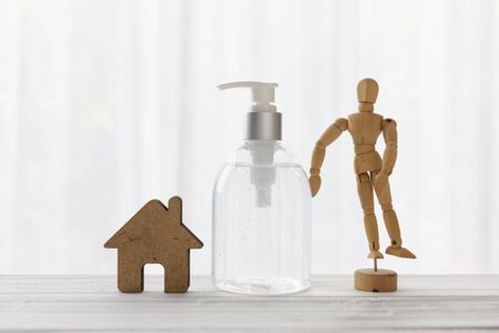 Hand sanitizer,house icon,wood doll  on wooden table with soft white background while Covid-19  home quarantine .の写真素材