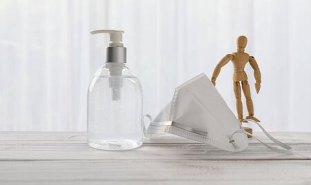 Hand sanitizer,surgical mask,wood doll  on wooden table with soft white background while Covid-19  home quarantine .の写真素材