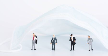 Miniture business people do social distancing under surgical mas on white background,due to  Pandemic coronavirus(COVID-19)  wear mask can save life conceptual.の写真素材