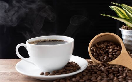 Steam coffee cup with roasted beans and flower pot on wood background in morning sunlightの写真素材