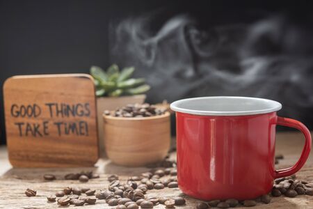 Steam coffee red cup with text,roasted beans and flower pot on wood background in morning sunlightの写真素材