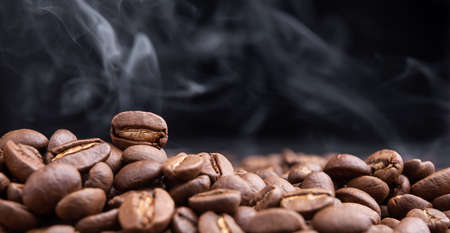 Aroma roasted coffee beans with smoke rising over dark backgroundの写真素材