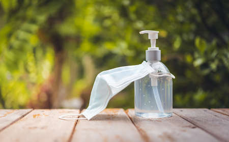 Face mask and white hand sanitizer or alcohol gel pump bottle on wooden top with green nature backgroundsの写真素材