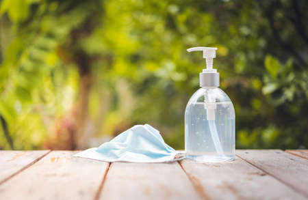 Face mask and white hand sanitizer or alcohol gel pump bottle  protection from coronavirus on wooden top with green nature backgroundsの写真素材