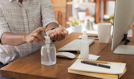 Female worker sit in home office use hand sanitizer against coronavirus pandemic work with computer and coffee on tableの写真素材