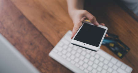 Woman hand holding credit card and mobile phone with computer for internet banking and online shopping concept.の写真素材